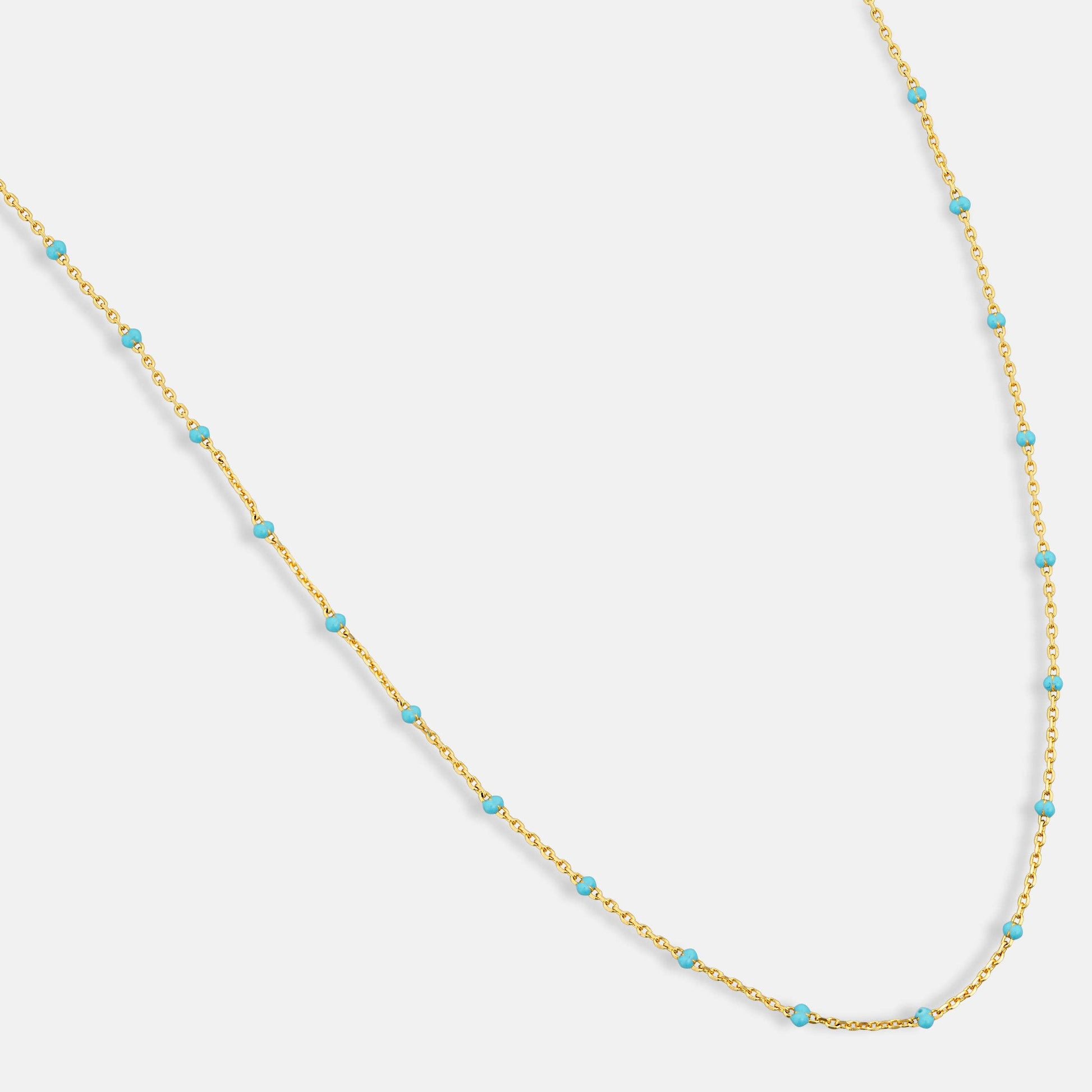 Gold necklace with turquoise beads on a light gray background