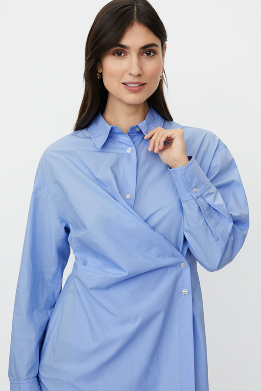 Oxford blue mid-length shirt dress with wrap detail and side buttoning. Classic collar and cuffs, a contemporary take on the shirt dress.